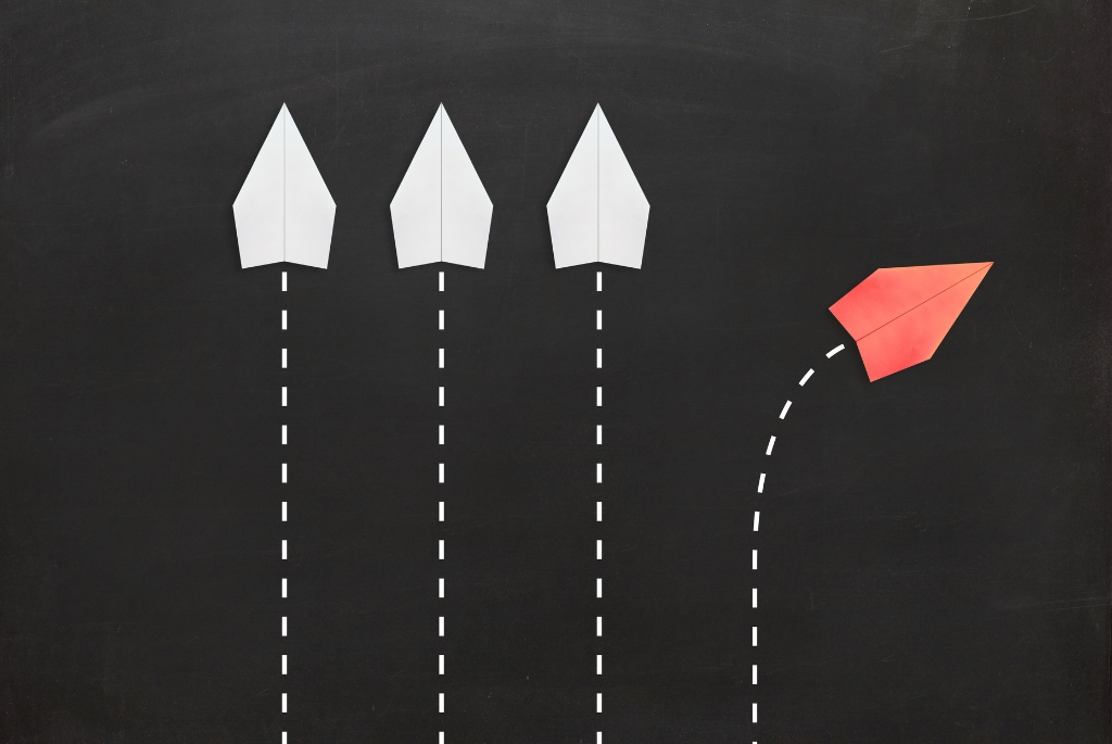 3 white paper airplanes going up, one red paper airplane going up and right